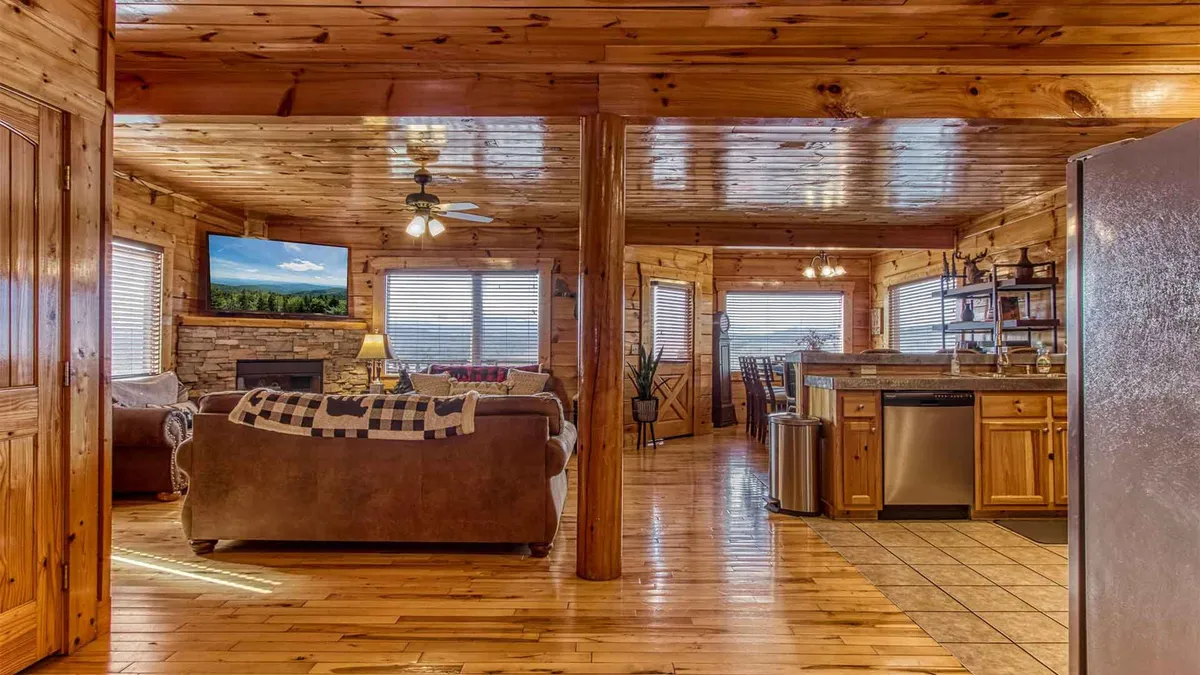 A wide-angle interior view that encompasses the living room, dining area, and kitchen. Wooden beams and rustic décor add to the cozy ambiance, while the comfortable couch, spacious dining table, and well-equipped kitchen with modern appliances seamlessly connect for effortless gathering and entertaining.