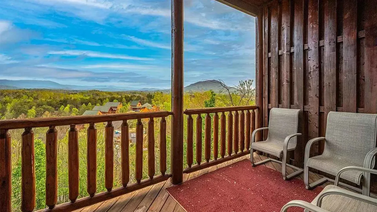 This exterior image captures a wooden deck with two chairs and a red rug overlooking breathtaking mountain views. The inviting setup suggests a perfect spot for couples to relax, enjoy a glass of wine, and take in the natural scenery.