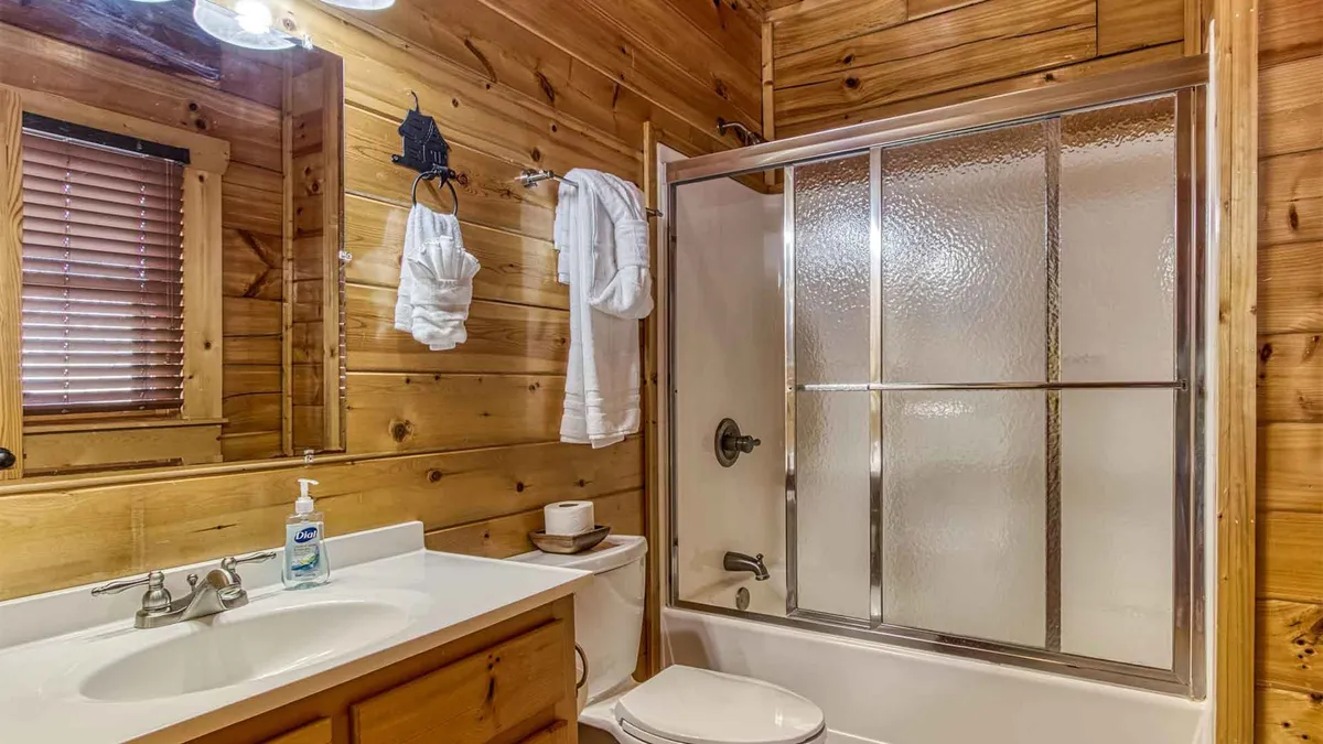 A modern bathroom with wooden walls, a glass shower enclosure, and plush white towels. The space is calm and spa-inspired, offering both functionality and peacefulness.