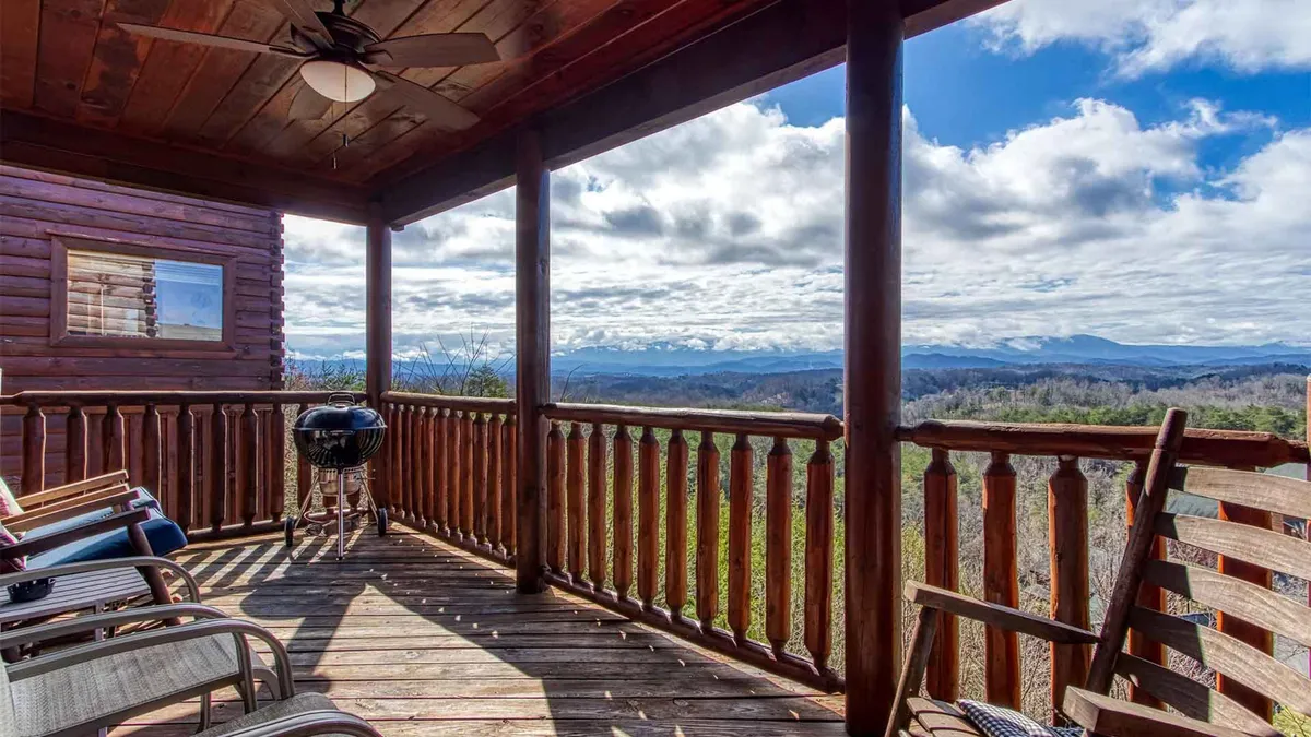 An inviting outdoor space with a wooden railing, ample outdoor seating, a grill, and an expansive view of the mountains. The area is set up for both relaxation and socializing, with plenty of room for friends or family to gather and soak in the scenery.