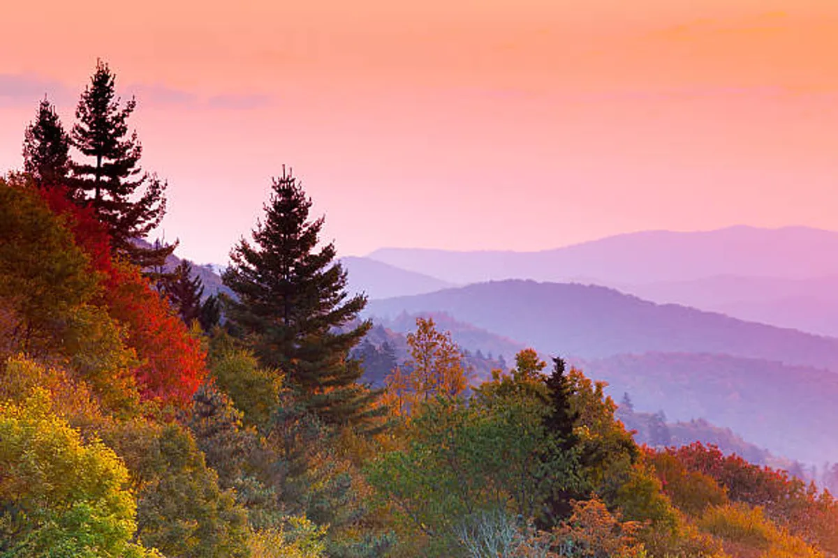 A breathtaking view of the Smoky Mountains with colorful sky hues at sunset, distant mountain ridges, and lush trees in the foreground. The image reflects the grandeur and beauty of the surrounding national park.