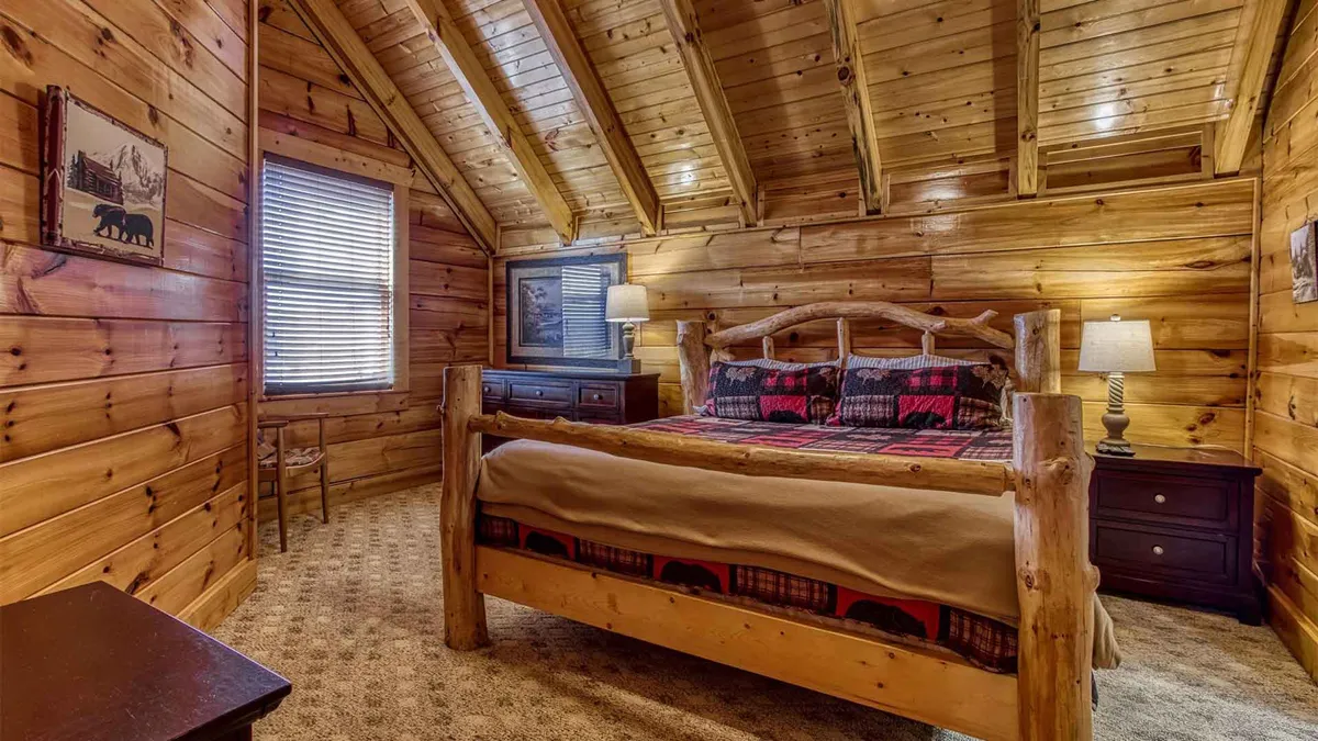 A cozy, warmly lit bedroom featuring a log bed with plaid bedding, wooden walls, and nightstands topped with lamps. The inviting space emphasizes warmth and comfort, ideal for relaxing after a day of adventure.