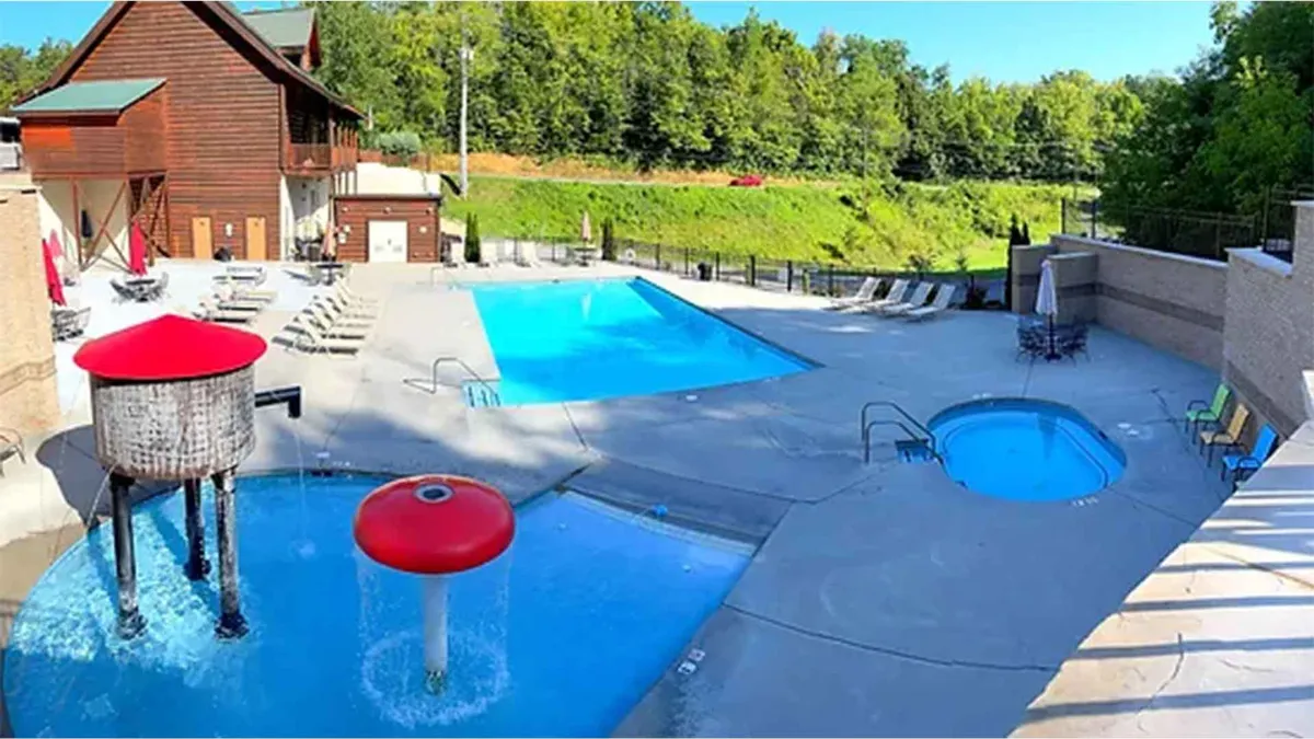 A vibrant exterior scene featuring a large community swimming pool with sparkling blue water, a smaller hot tub, a playful mushroom-shaped water feature ideal for children, and an array of comfortable lounging chairs surrounding the pool deck. The area is well-maintained and bathed in cheerful natural light, signaling an inviting atmosphere for both family relaxation and play.