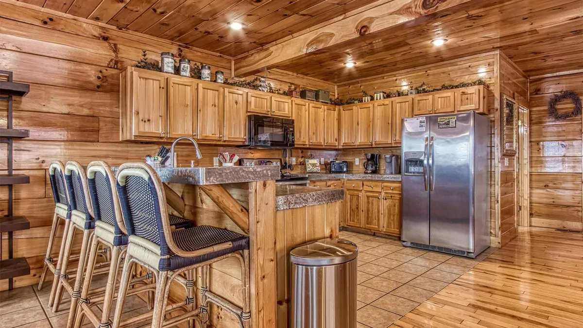 A close-up of the modern kitchen, showcasing wooden cabinetry, bar stools at a granite countertop, and gleaming kitchen appliances. The space feels both functional and inviting, ideal for cooking, entertaining, and sharing special meals.