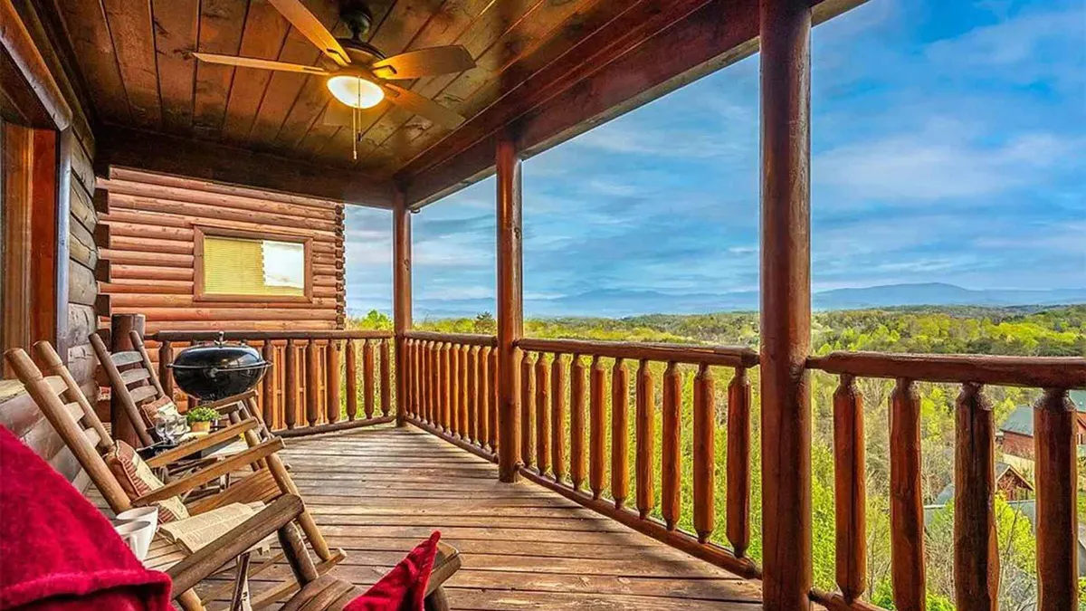 A wooden deck with log railings features rocking chairs, a grill, and distant mountain views. The setting is tranquil, ideal for barbecues, socializing, and enjoying sunsets, encapsulating the blend of nature and comfort.